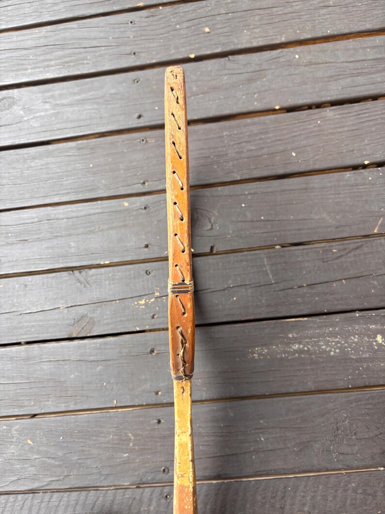 May include: A wooden tennis racket with a brown leather grip and stitching. The racket is made of wood and has a natural finish.