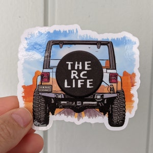 Puede incluir: Una pegatina de un Jeep gris conduciendo por un camino con una rueda de repuesto negra que dice "THE RC LIFE" en letras blancas. El fondo es una pintura de acuarela de un cielo azul con nubes y árboles naranjas.