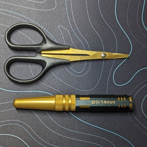 May include: A black and gold pair of small scissors with a gold handle and a black blade.  A gold and black metal tool with the text "0-14mm" on the side.