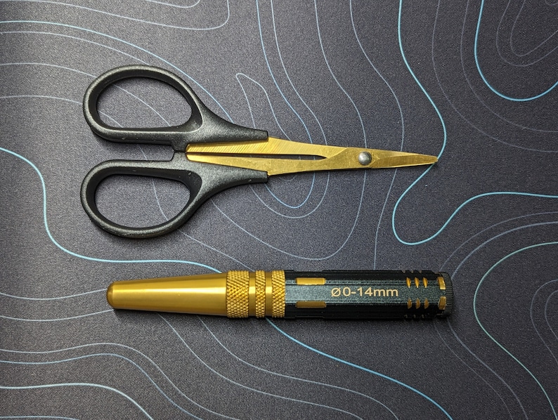May include: A black and gold pair of small scissors with a gold handle and a black blade.  A gold and black metal tool with the text "0-14mm" on the side.