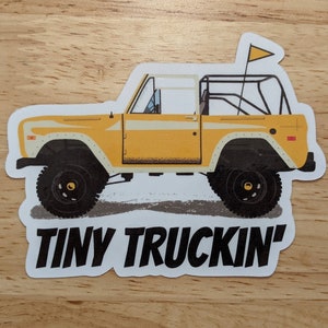 Könnte beinhalten: Ein gelber Vintage-Truck-Aufkleber mit schwarzem Umriss und dem Text "TINY TRUCKIN'" unter dem Truck.