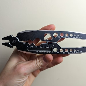 May include: A silver and black multi-tool pliers with a variety of sizes for nuts and bolts. The tool has markings for 78, 6.2, 5.0, 4.6, 2.7, 2.4, 3.5, 38, 35, 30, 22, 18, 12, 8, 25, 20, 15, 10, 5, 6.9, 5.8, 5.3, 4.3, 3.2, and 2.0.