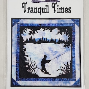May include: A blue and white quilt pattern with the title "Tranquil Times" and a silhouette of a person fishing in a lake with trees in the background.