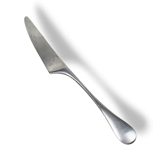May include: A single, stainless steel butter knife with a rounded tip and a long, curved handle. The blade shows signs of wear, with a slightly textured surface. The knife is set against a white background, casting a shadow.