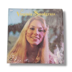 May include: A vinyl record album cover featuring a portrait of Virginia Snodgrass, a blonde woman with a bright smile. The album title is "Virginia Snodgrass" in yellow lettering.