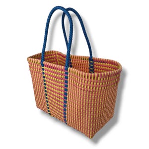 May include: A rectangular woven tote bag featuring a vibrant checkerboard pattern in bright pink and yellow. The bag includes two sturdy, braided blue handles that extend down the sides, providing structural support and a contrasting color accent.