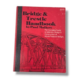 May include: A red softcover book titled Bridge & Trestle Handbook by Paul Mallery. The cover features a black line drawing of a truss bridge and the subtitle The Complete Guide to Selection, Design, & Construction of Model Railroad Bridges.