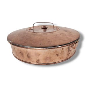 May include: A vintage copper cooking pot with a lid and handle. The pot has a round shape with a slightly oval lid. The copper has a warm, reddish-brown color with some signs of wear, suggesting age and use. The handle is a simple loop.