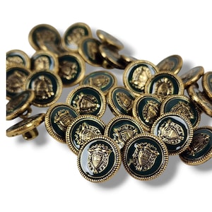 Puede incluir: Una colección de botones redondos y decorativos. Los botones tienen un centro verde oscuro con un emblema dorado y un borde dorado en forma de cuerda. Los botones están dispersos sobre una superficie blanca.