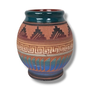 May include: A rounded ceramic vase featuring a dark teal rim and base. The body displays horizontal bands of terracotta clay with etched geometric patterns, including a central Greek key design and triangular motifs in shades of blue and brown.