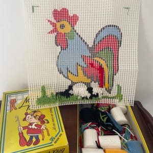 May include: A vintage "My First Rug" latch hook kit with a colourful rooster design. The kit includes a canvas, yarn, and a hook, with the text "...it's as easy as tying" on the box. The rooster is blue, red, yellow, and green.