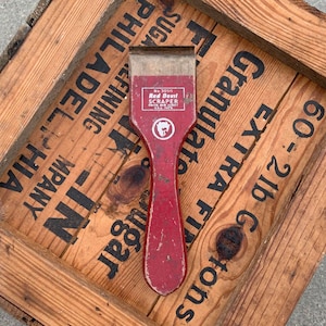 May include: Red Devil scraper with a red wooden handle and a black and white logo. The scraper is labeled "Red Devil Scraper" and "No. 3050".