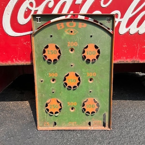 May include: A vintage green metal game board with the word "BOP" in orange letters. The board has various orange circles with numbers on them, including 25, 100, 200, 250, 300, 350, 500, and "OUT".