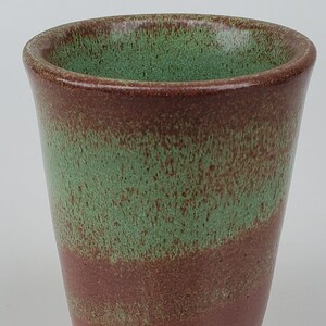 May include: A green and brown ceramic mug with a speckled glaze.