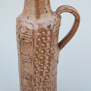 May include: A brown and pink ceramic pitcher with a textured surface and a handle. The pitcher has a narrow neck and a wide base.