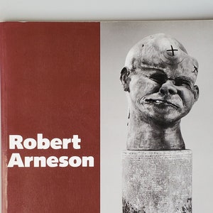 May include: A book cover with a red background and the text "Robert Arneson" in white. The cover also features a black and white photograph of a ceramic sculpture of a person's head.