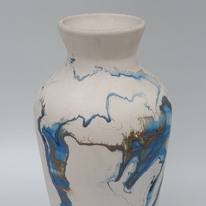 May include: White ceramic vase with blue and gold marbling. The vase has a rounded body and a narrow neck.