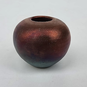 May include: A spherical, iridescent vase with a textured surface. The vase transitions from a deep burgundy at the top to a teal-green at the base. The opening is a dark brown color.