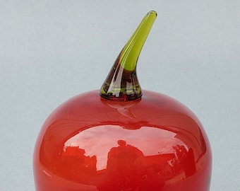 May include: A red glass apple with a green glass stem. The apple is shiny and has a smooth surface.
