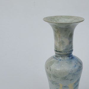 May include: A light blue and white ceramic vase with a flared top and a textured surface.