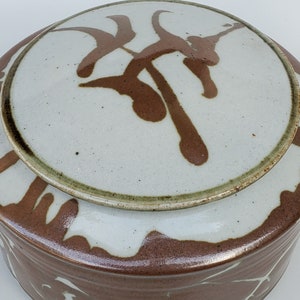 May include: A ceramic jar with a lid, both decorated with brown abstract designs on a white background.