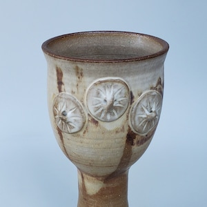 May include: A ceramic goblet with a brown and white glaze. The goblet has three raised circular designs on the side.