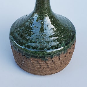 May include: A green and brown ceramic vase with a narrow neck and a wide base. The vase has a textured, speckled glaze.
