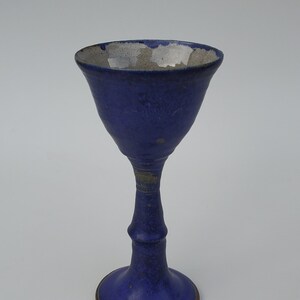 May include: A blue ceramic goblet with a white rim and a flared base. The goblet has a textured surface and a slightly uneven glaze.