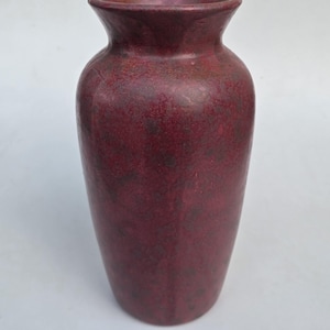 May include: A vase with a flared rim and a rounded body, featuring a deep burgundy and dark red mottled glaze finish. The surface displays a textured, speckled appearance with varying shades of red and dark purple throughout the entire exterior.