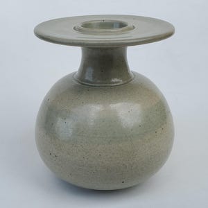 May include: A light green ceramic vase with a round body and a wide, flat top. The vase has a speckled glaze.