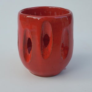 May include: A red ceramic planter with a unique design featuring vertical cutouts. The planter has a smooth, glossy finish.