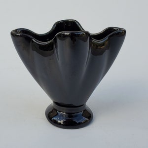 May include: A black ceramic vase with a ruffled, flared top and a round base.
