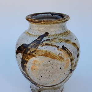 May include: A ceramic vase with a white glaze and brown and orange abstract designs. The vase has a round body and a narrow neck.
