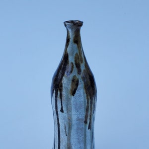 May include: A white ceramic vase with brown and black glaze dripping down the sides. The vase has a narrow neck and a wide base.