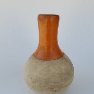 May include: A wooden vase with a light brown body and a dark brown top. The vase has a rounded bottom and a narrow neck.