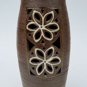 May include: A brown ceramic vase with two white cutout flower designs. The vase has a textured surface.
