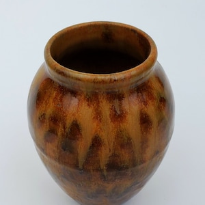 May include: A small, round, brown ceramic vase with a mottled glaze. The vase has a wide opening and a rounded bottom.