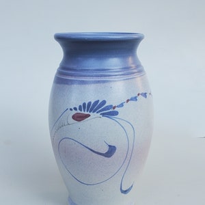 May include: A white ceramic vase with a blue and purple glaze. The vase has a unique design with a swirl pattern and a flower-like design in blue and red.