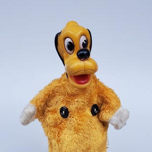 Peut inclure: Un chien en peluche jaune portant une combinaison jaune avec des boutons noirs et des poignets blancs. Le chien est assis sur une bouteille en verre de jus de raisin.