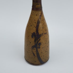 May include: A brown ceramic vase with a black rim and a black floral design. The vase has a speckled texture.