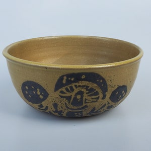 May include: A brown ceramic bowl with a black and white design of stylized mushrooms. The bowl has a rounded shape and a slightly flared rim.