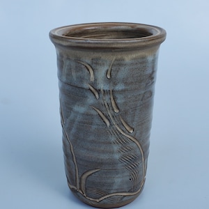 May include: A ceramic vase with a light brown glaze and a white glaze with a design of stylized leaves and branches.