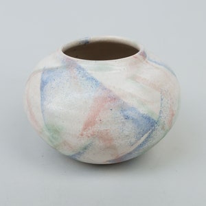 May include: A white ceramic vase with a rounded shape and a colorful abstract design in shades of blue, green, and pink.