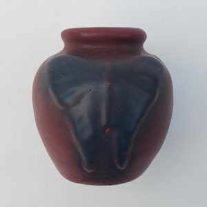 May include: A small, dark red ceramic vase with a blue butterfly design. The vase is approximately 10 cm tall and has a rounded shape.