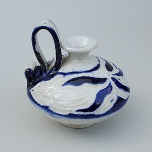 May include: A small white ceramic pitcher with a blue and white floral design. The pitcher has a handle and a spout.