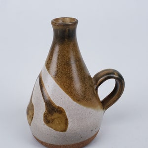 May include: A small, brown and white ceramic vase with a handle. The vase has a unique, abstract design with brown and white swirls.