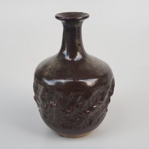 May include: A dark brown ceramic vase with a textured surface and a narrow neck.