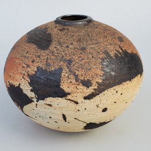 May include: A round ceramic vase with a speckled brown, orange, and white glaze. The vase has black splatter paint accents.