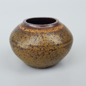 May include: A small, round, brown and yellow ceramic vase with a speckled glaze.