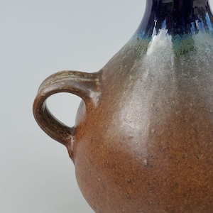 May include: A brown ceramic vase with a blue and green glaze. The vase has a rounded body and a single handle.